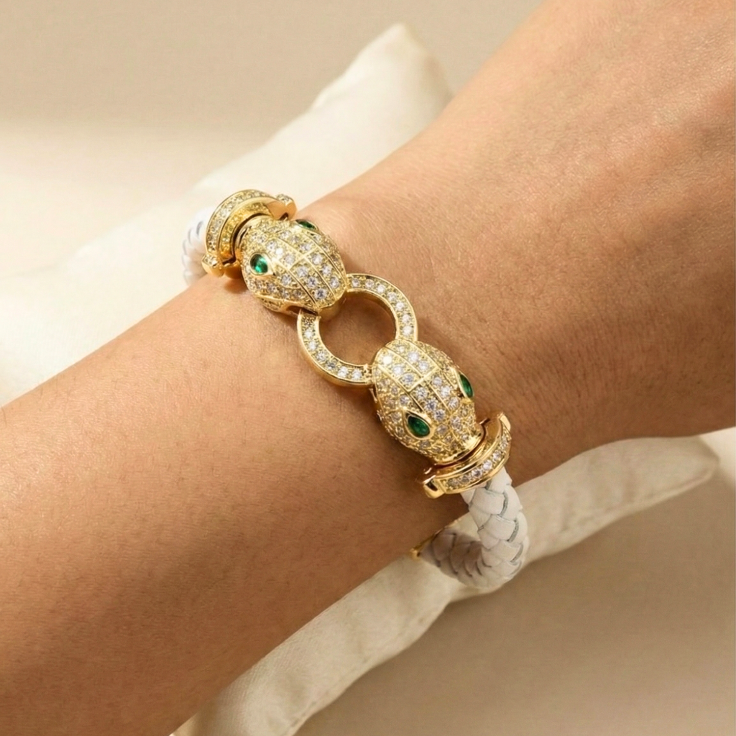 Gold bracelet with emerald and diamond accents on a wrist against a neutral background Snake bracelet, braided leather jewelry, serpent head bracelet, gold snake jewelry, pavé crystal bracelet, luxury leather accessories, twin serpent bracelet, emerald eye jewelry, statement jewelry 2026, designer style leather bangle.