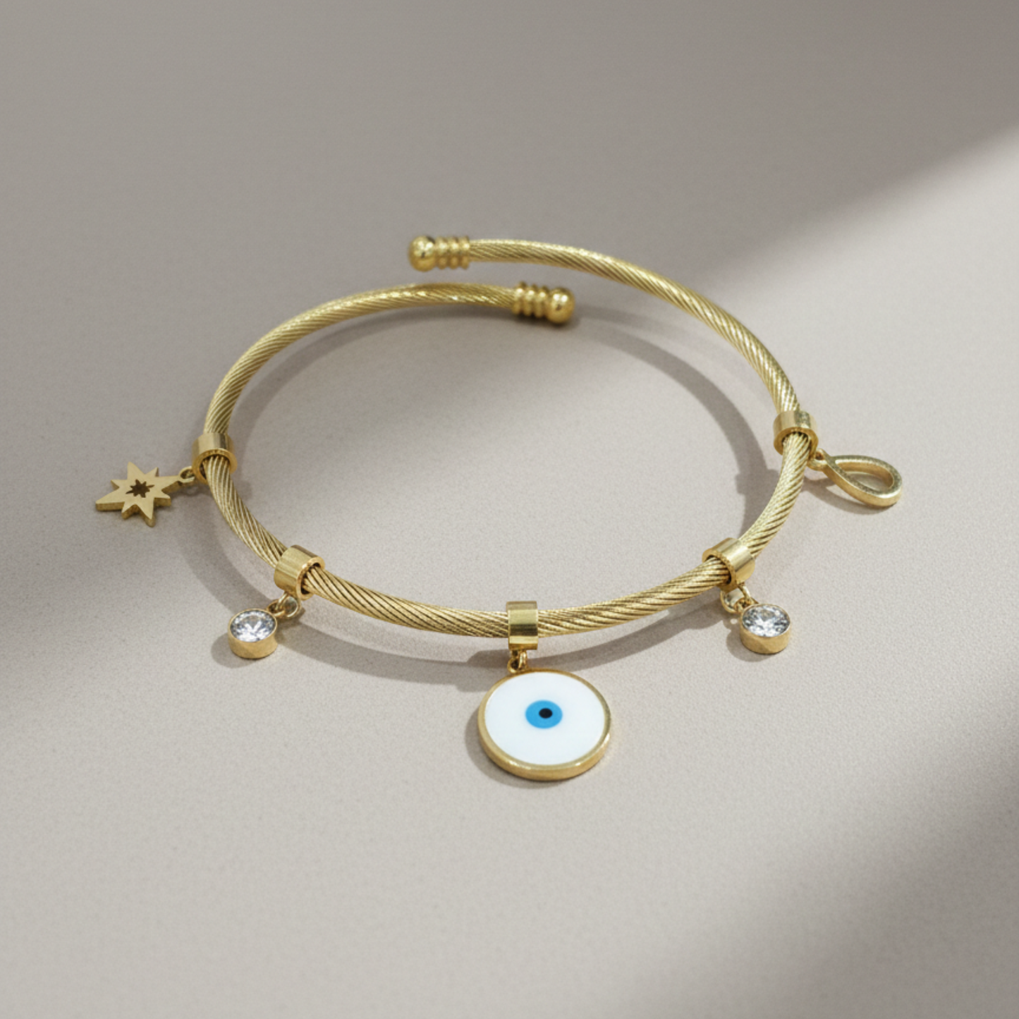 Gold bracelet with charms on a beige background Evil eye bracelet, gold cable bangle, nazar jewelry, celestial charm bracelet, spiritual protection jewelry, gold cuff bracelet, adjustable jewelry for women, twisted cable bracelet, star charm bangle.