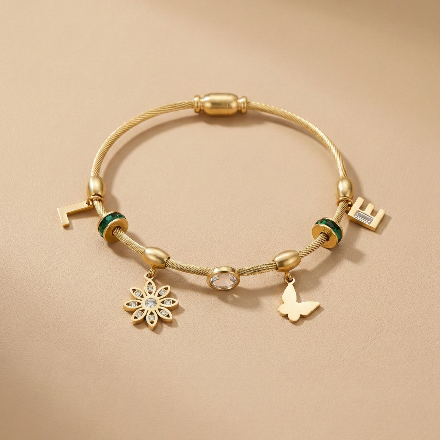 Gold bracelet with various charms on a beige background Gold cable bracelet, charm bangle for women, butterfly charm jewelry, floral gold bracelet, emerald green crystal jewelry, personalized initial bracelet, luxury cable bangle, women's fashion accessories, stackable gold jewelry.