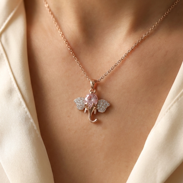 Necklace with a decorative pendant featuring a pink gemstone and floral elements on a person wearing a beige garment. Elephant necklace, rose gold pendant, pink crystal jewelry, lucky charm necklace, dainty gold jewelry, Tiknarah jewelry, women's fashion necklace, symbolic jewelry gift, animal pendant necklace, pink stone necklace.