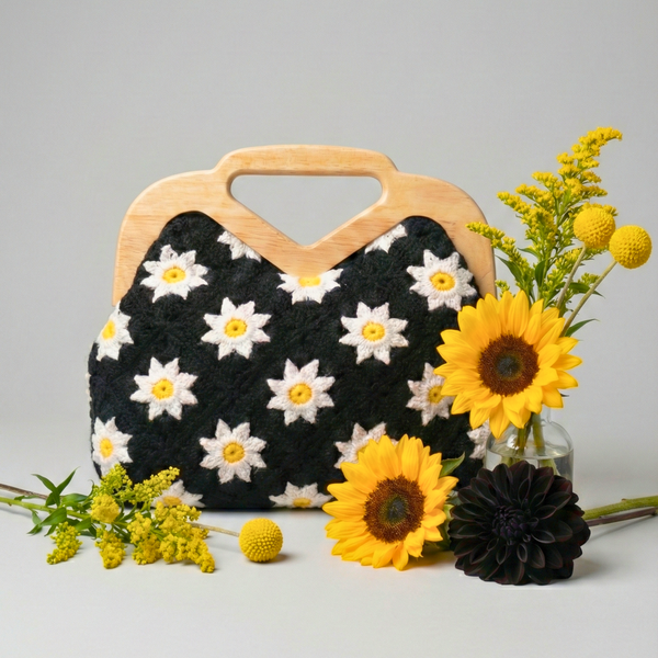 Handbag with floral pattern and wooden handle surrounded by sunflowers on a light gray background Handmade crochet bag, daisy knit clutch, wooden handle handbag, boho-chic accessories, artisanal knitwear, Tiknarah boutique, floral crochet purse, vintage style handbag, summer clutch bag.