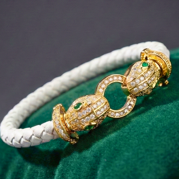 Gold bracelet with intricate design on a white cord against a green background Serpent Bracelet, Leather Snake Bangle, Crystal Serpent Jewelry, Emerald Eye Snake, Twin Snake Bracelet, Braided Leather Accessory, Luxury Statement Bracelet.