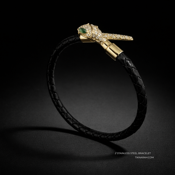 Black leather bracelet with gold clasp featuring a green gemstone on a dark background. Snake bracelet, braided leather jewelry, serpent head bracelet, gold snake jewelry, pavé crystal bracelet, luxury leather accessories, twin serpent bracelet, emerald eye jewelry, statement jewelry 2026, designer style leather bangle.